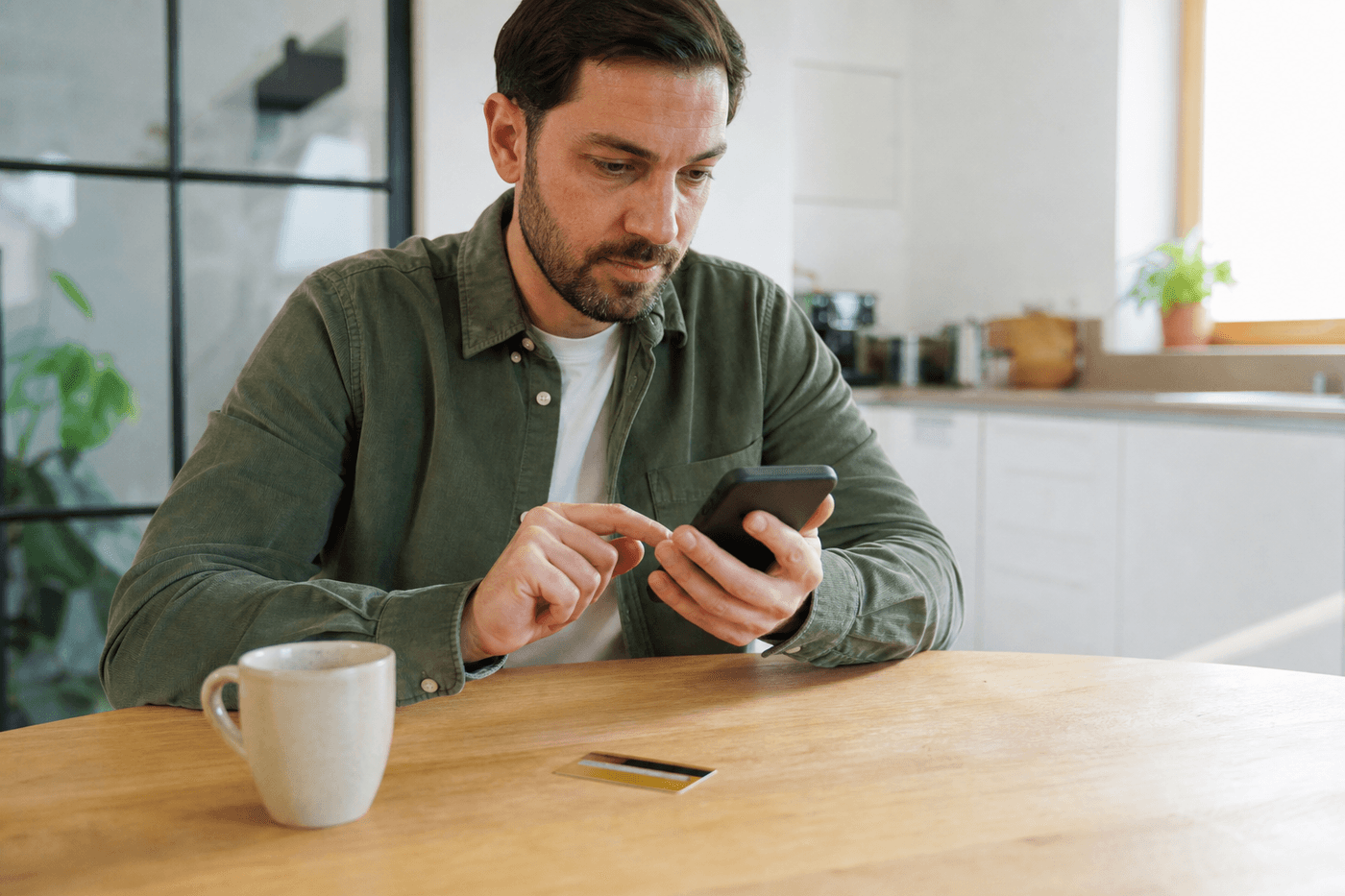 Personne consultant son application bancaire sur smartphone à une table, carte bancaire posée à côté