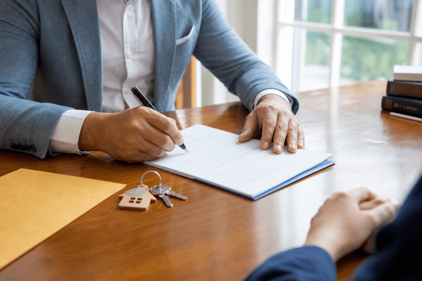 Personne signant des documents immobiliers sur une table en bois, clés et enveloppe de lettre recommandée posées à côté