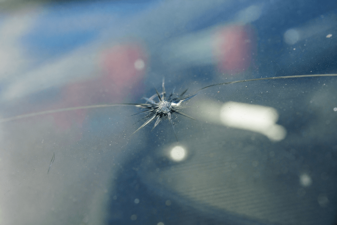 Gros plan sur un impact en forme d'étoile sur un pare-brise de voiture, avec une fissure qui part du point d'impact