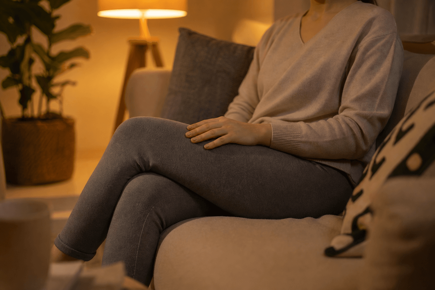 Une personne assise sur son canapé le soir, la main posée sur sa jambe, dans une ambiance domestique tamisée